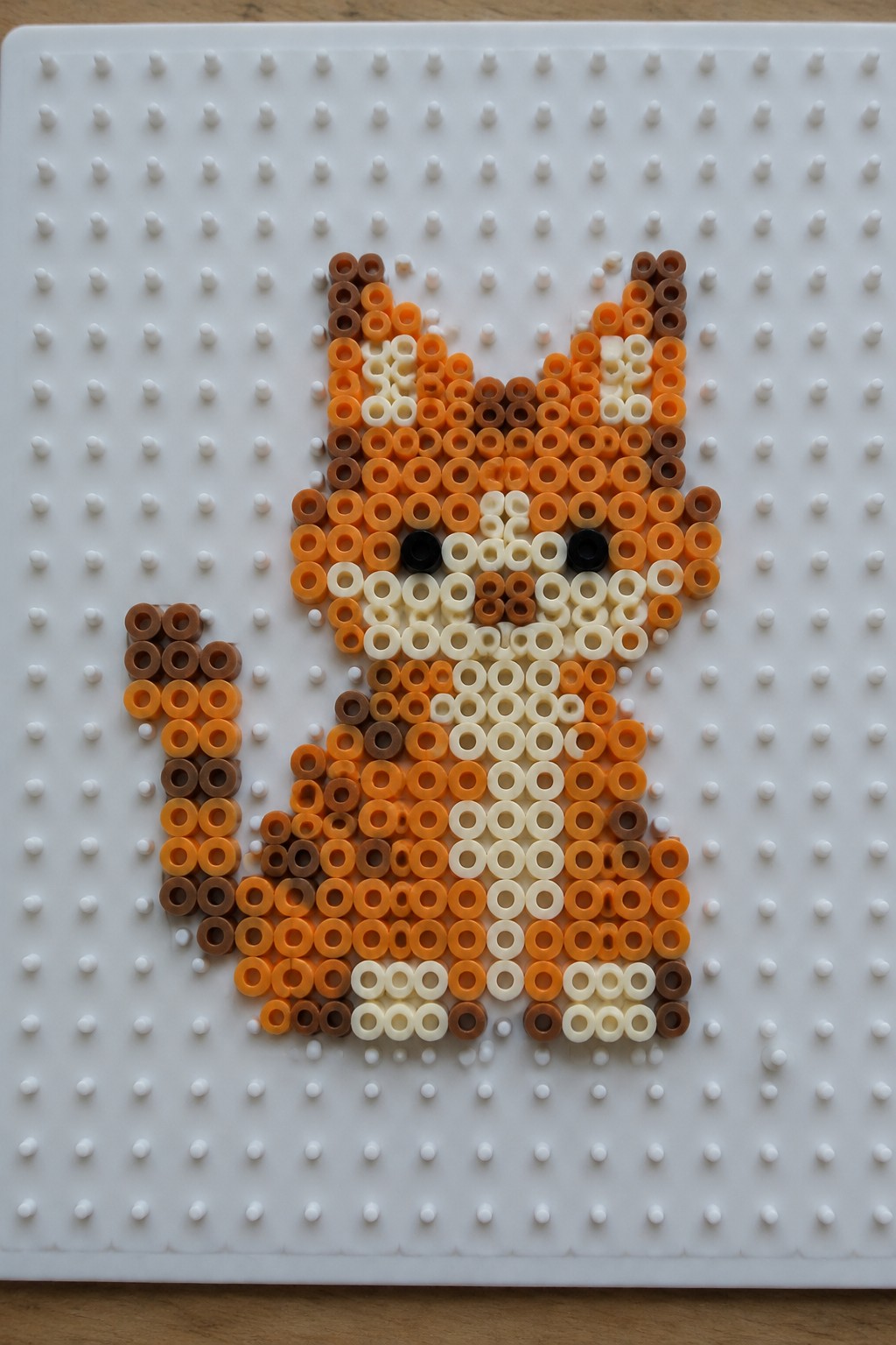 Perler bead fox in orange and brown shades on white pegboard.