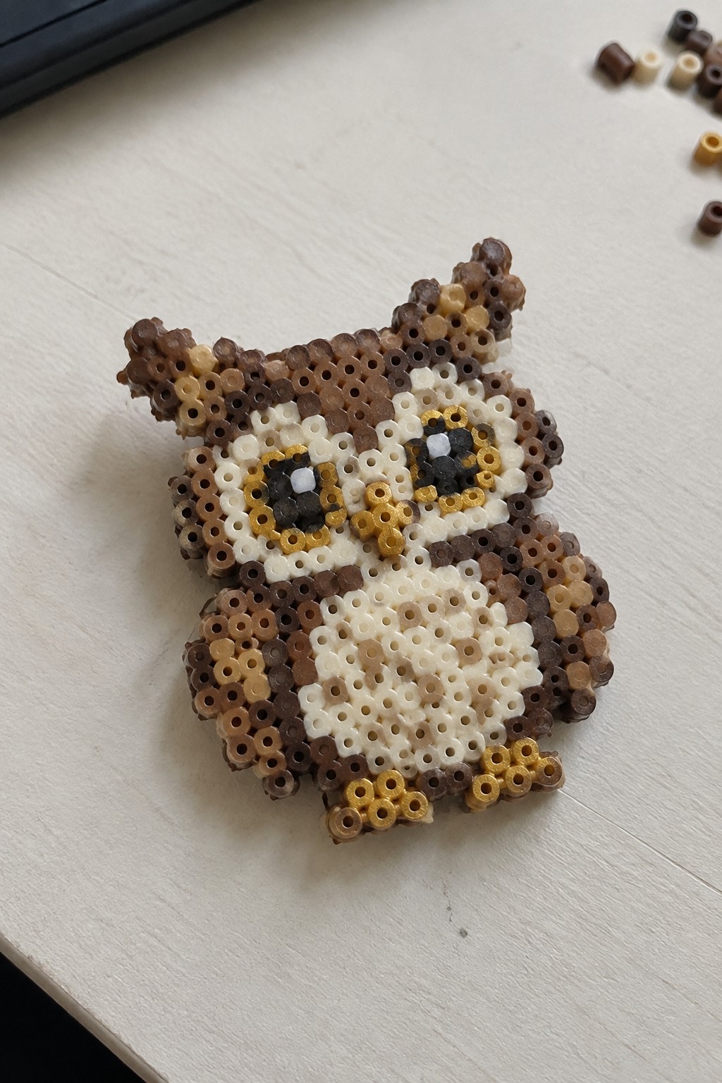 Perler bead owl craft in brown, white, and yellow beads on white surface