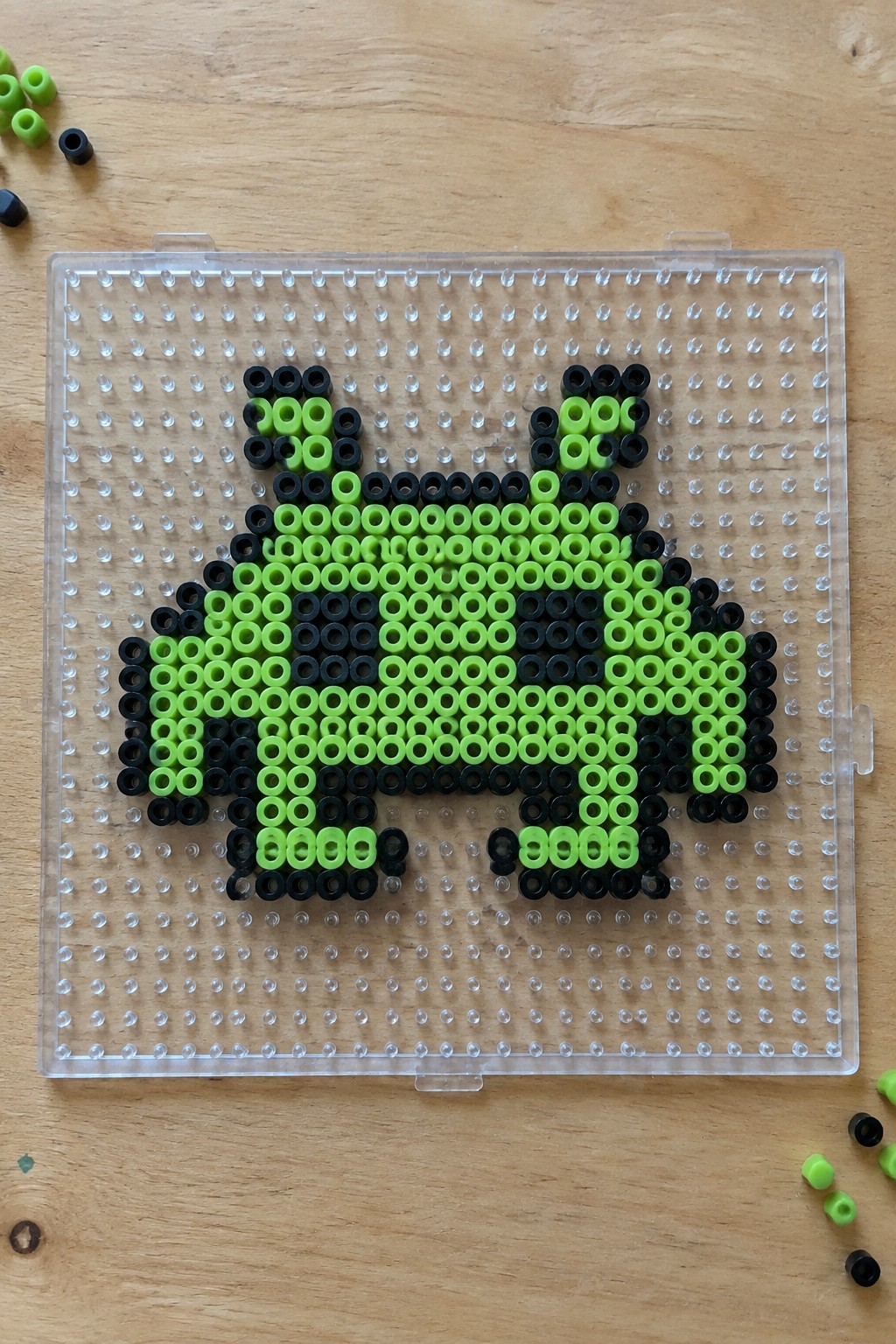 Neon green and black perler beads forming a cat on a clear pegboard