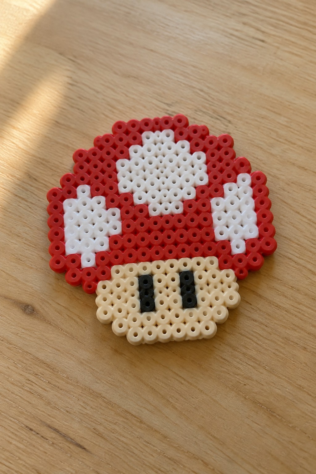 Red and white perler bead mushroom with black eyes on wooden table